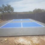 A blue and white tennis court with a concrete patio in a backyard.