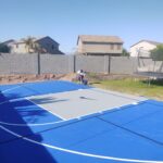 A backyard basketball court with a trampoline and a concrete patio area.