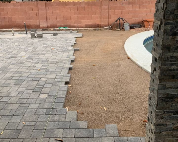 A pool with brick pavers and a concrete sidewalk in the background.