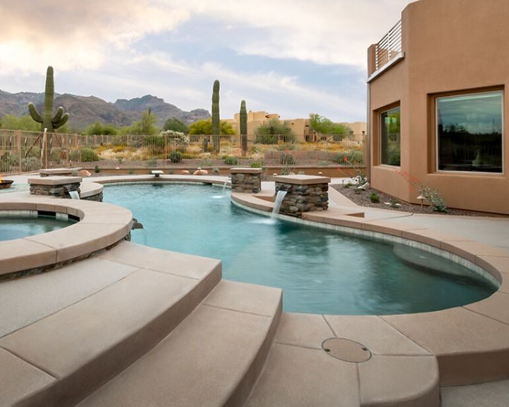 A pool in a desert setting with mountains in the background, featuring a concrete driveway.