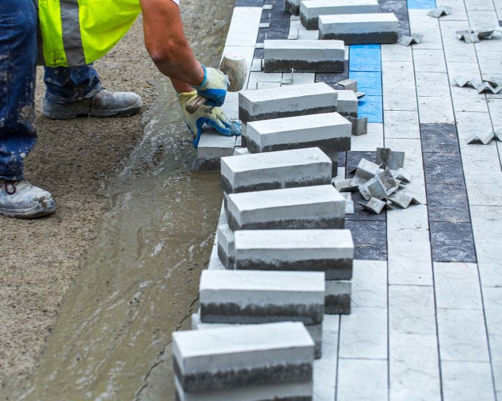 A worker is laying bricks on a concrete sidewalk.