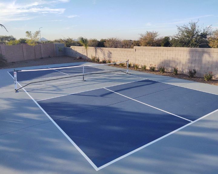A blue and white tennis court with a stamped concrete sidewalk in a backyard.